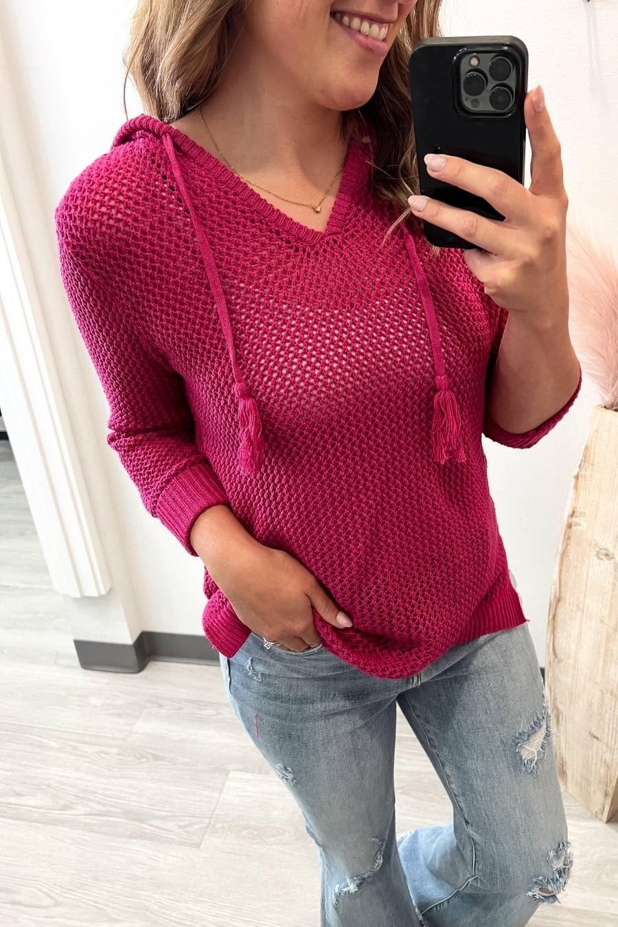 Person wearing a pink knitted hoodie and jeans, taking a mirror selfie.