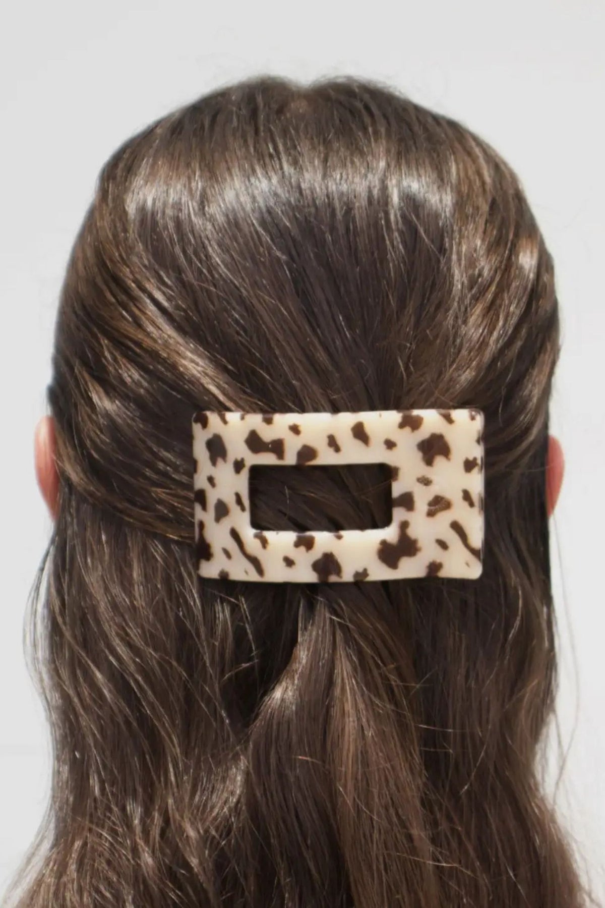 Person with a leopard print hair clip in their hair against a plain background