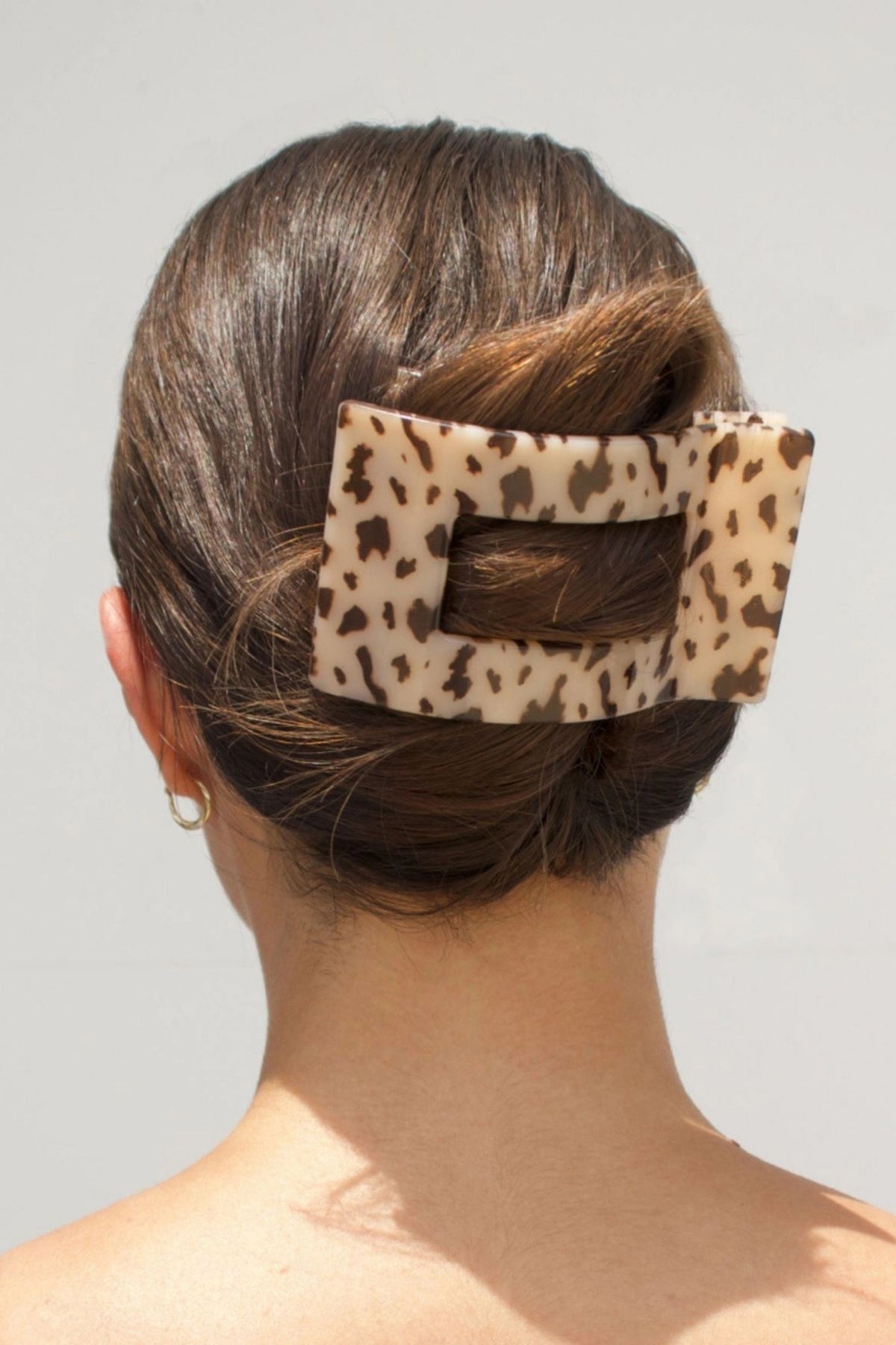 Person with a tortoise print hair clip in their bun against a neutral background