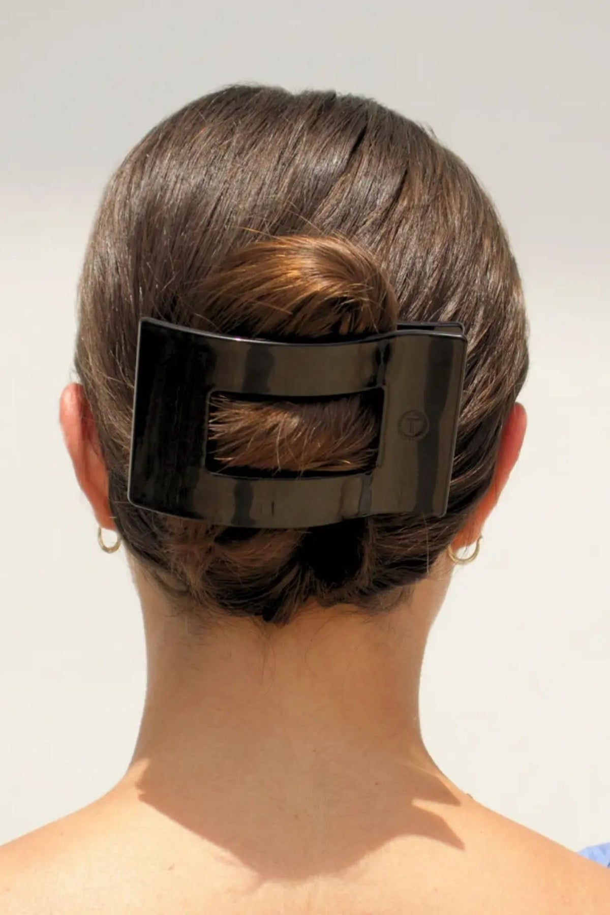 Person with a large black hair clip in their hair against a plain background