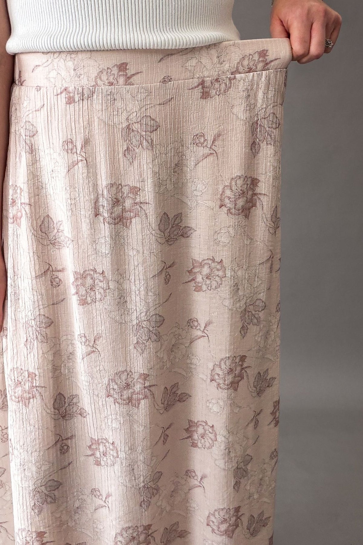 Woman wearing a blush floral midi skirt with elastic waistband  showing stretch in the waistband