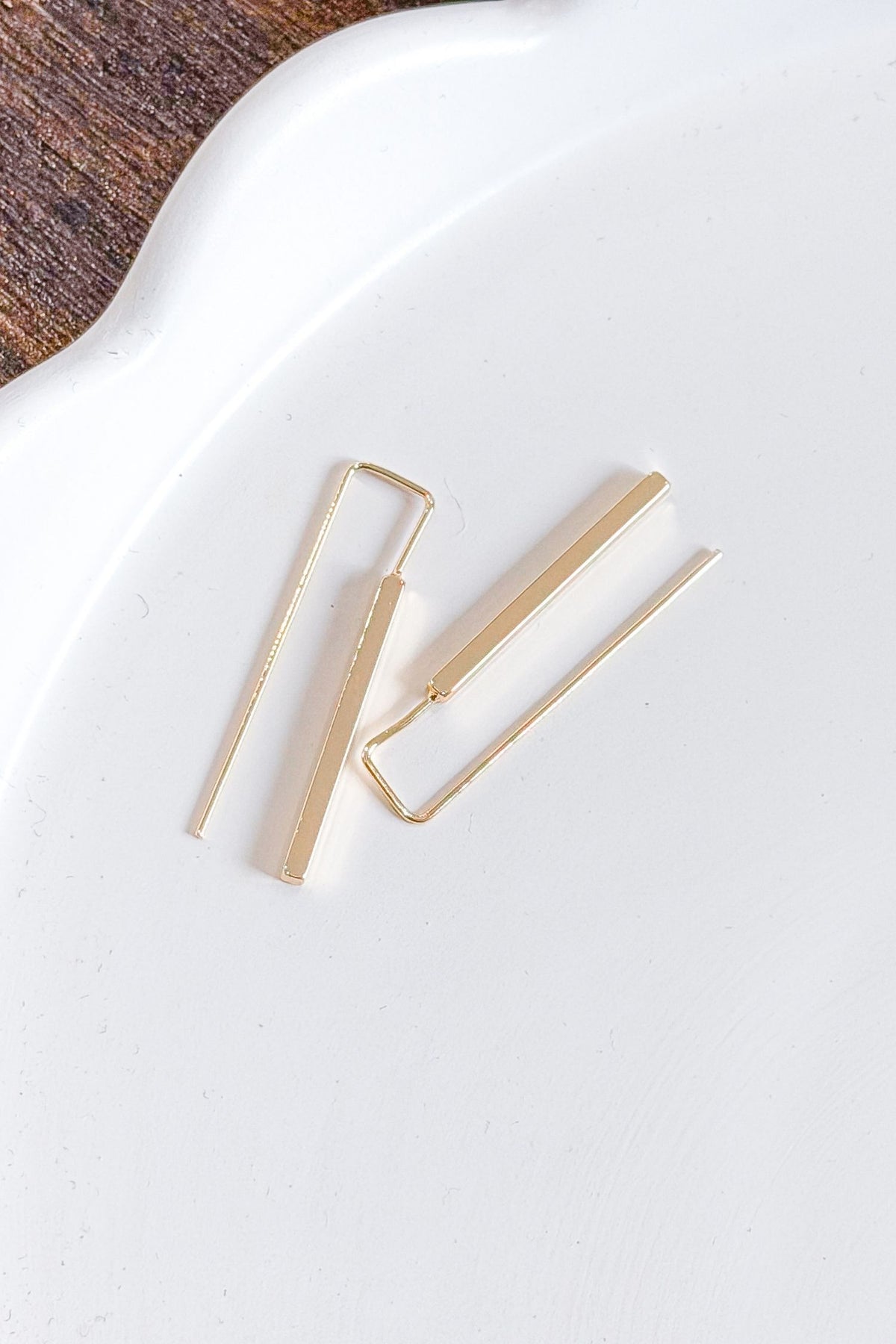 Gold hoop earrings on a white surface with a wooden background