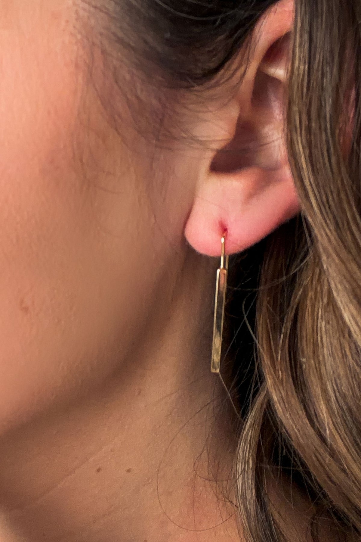 Close-up of a gold earring worn by a person with brown hair.