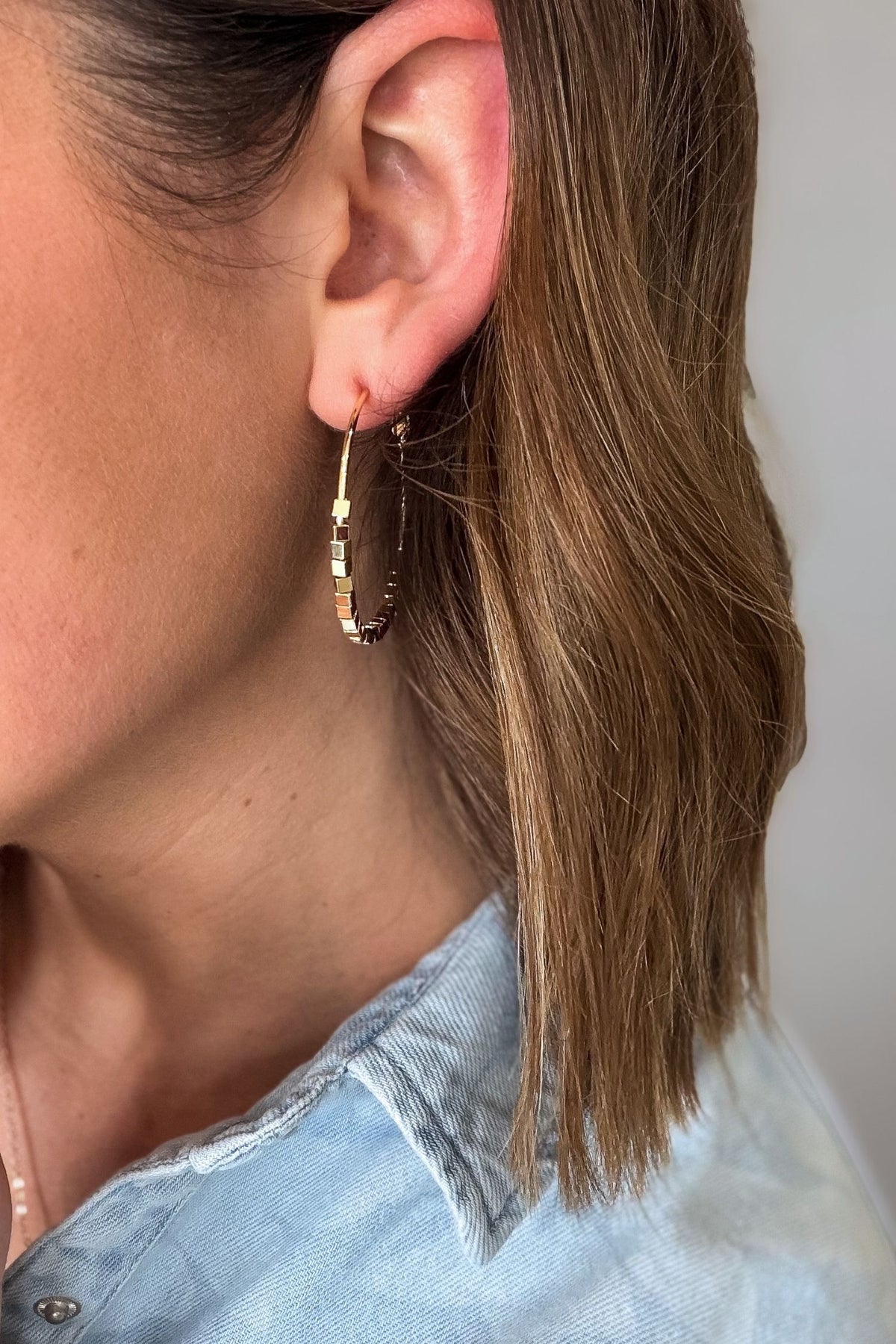 Close-up of a person wearing gold hoop earrings with a light blue shirt.