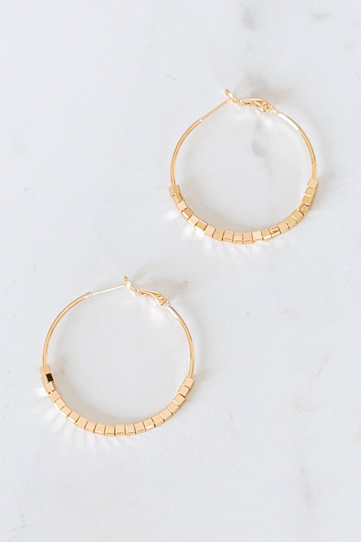 Gold hoop earrings with a textured design on a white background