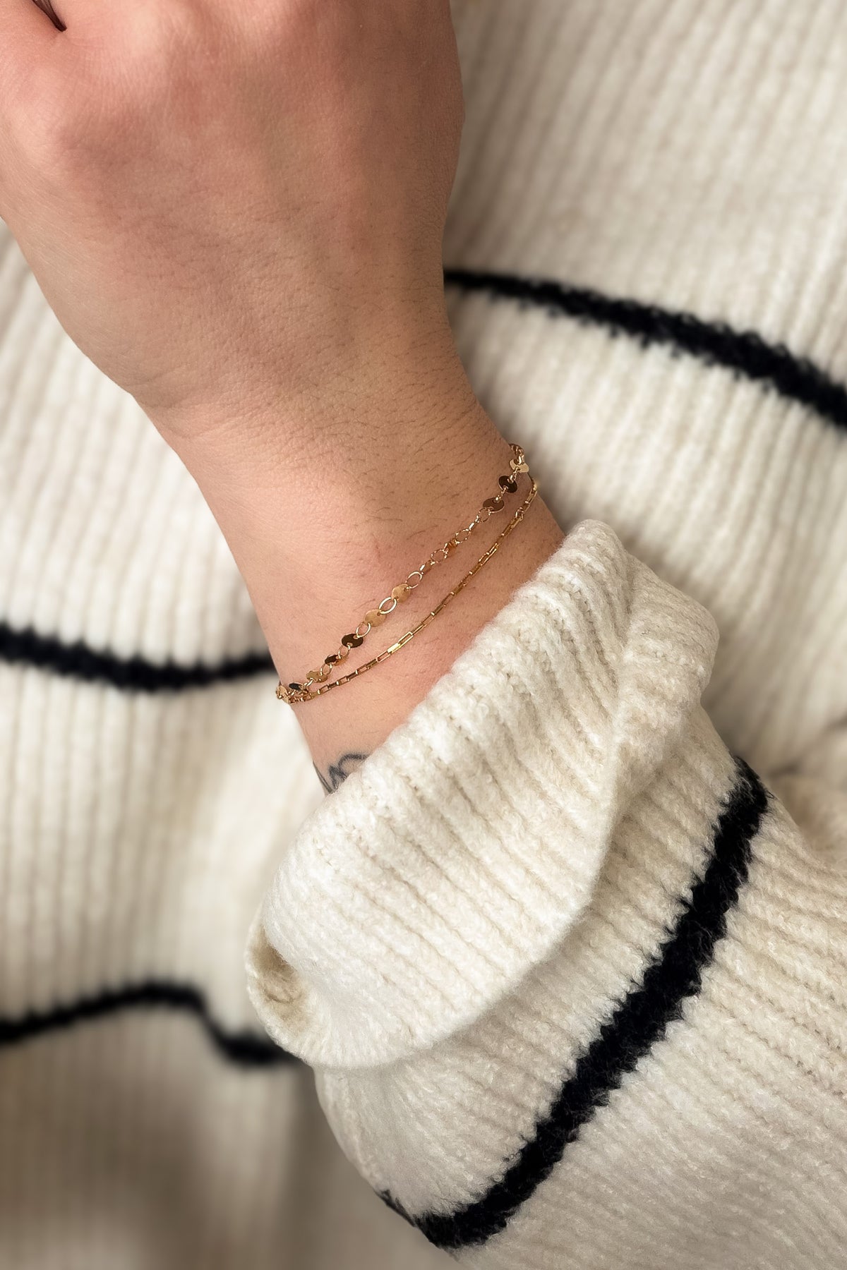 Close-up of a person wearing a gold bracelet on a white sweater with black stripes.