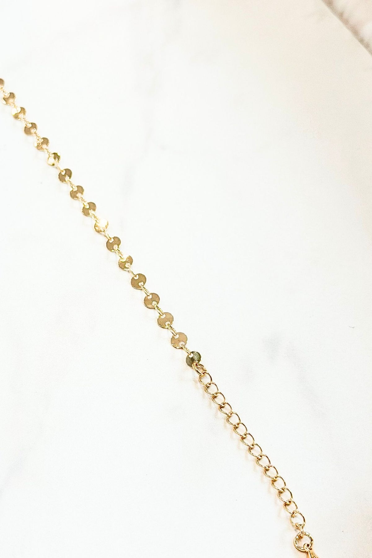 Gold necklace with alternating beads and chain on a white background