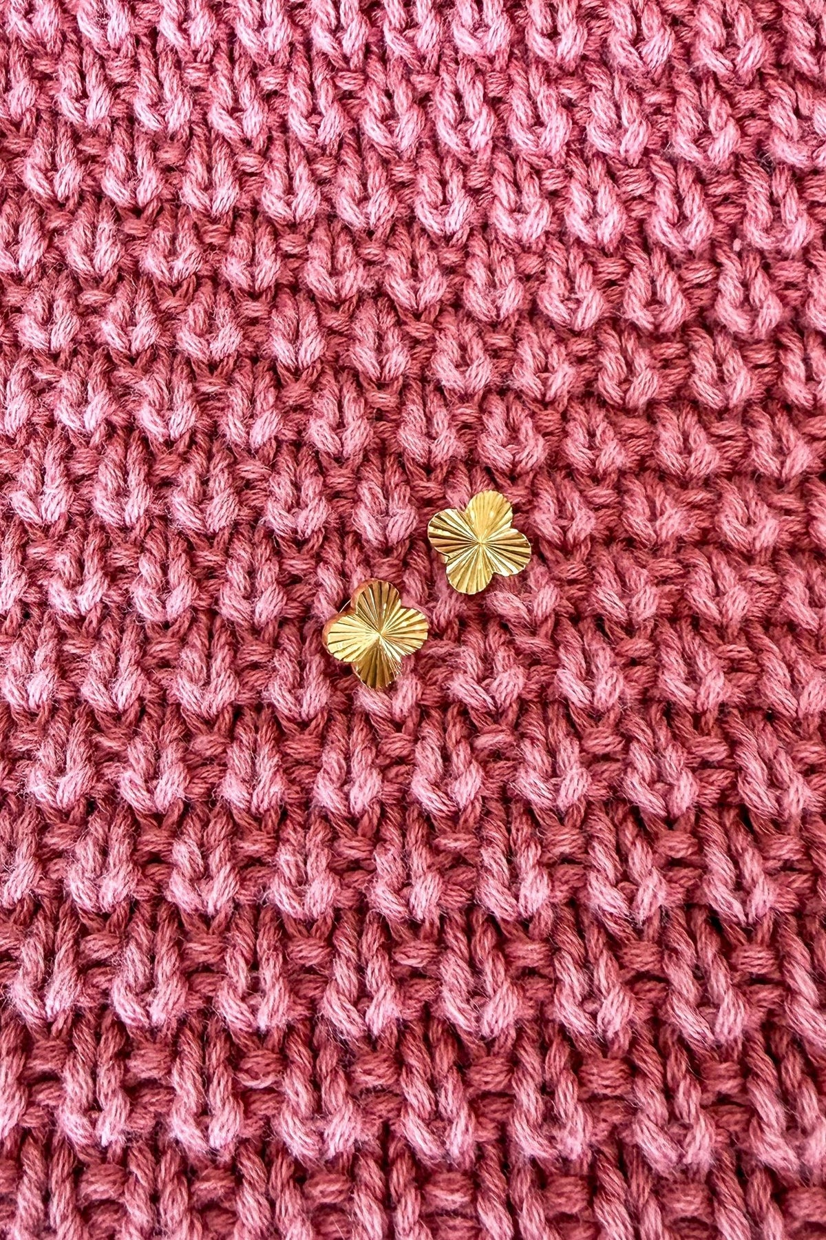 Close-up of pink knitted fabric with gold earrings on a textured background