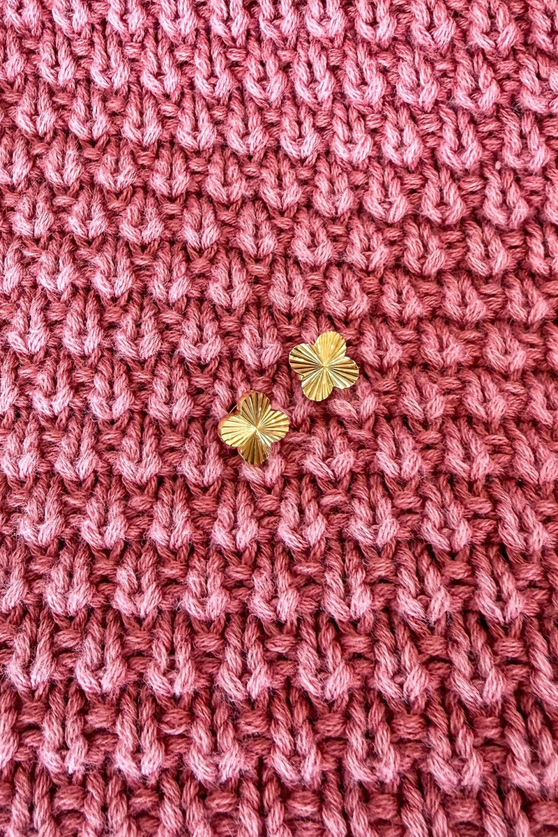 Close-up of pink knitted fabric with gold earrings on a textured background