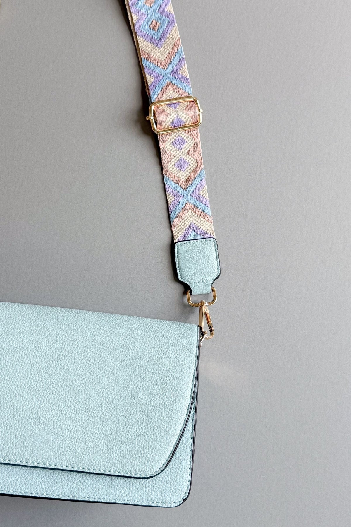 womens light blue handbag with a purple, taupe and blue patterned adjustable guitar strap on a grey background