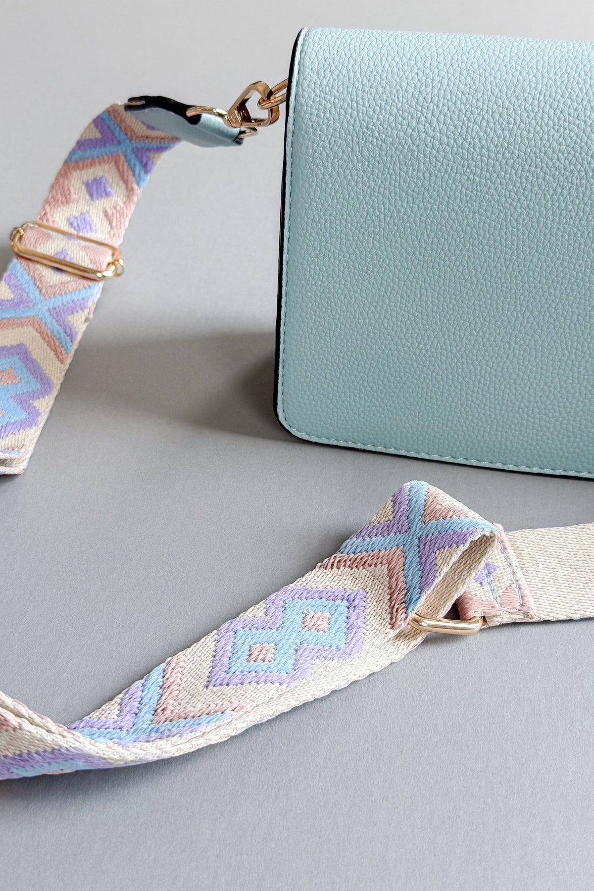 womens light blue handbag with a purple, taupe and blue patterned adjustable guitar strap on a grey background