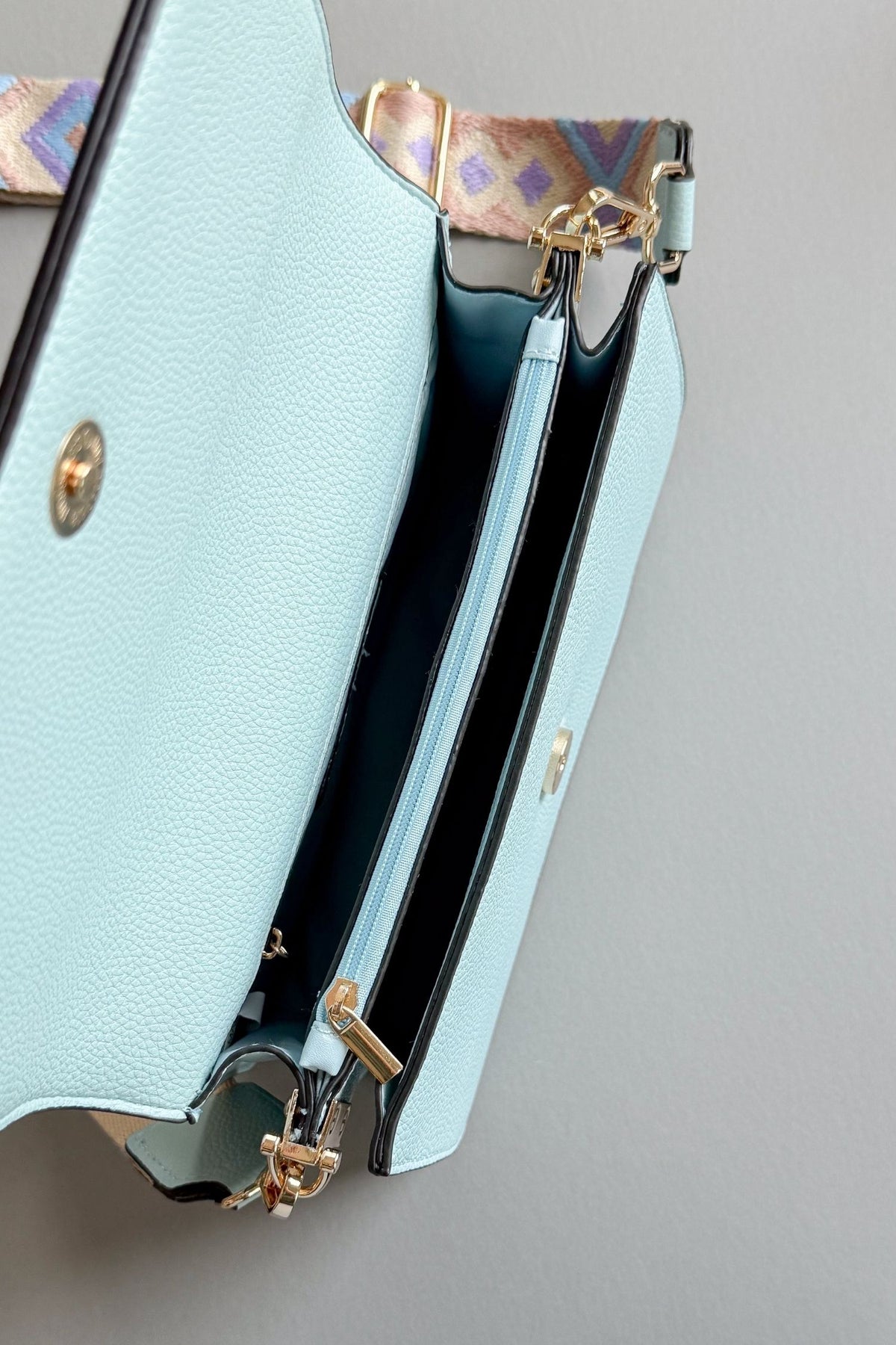 womens light blue handbag with a purple, taupe and blue patterned adjustable guitar strap on a grey background with a magnetic button closure