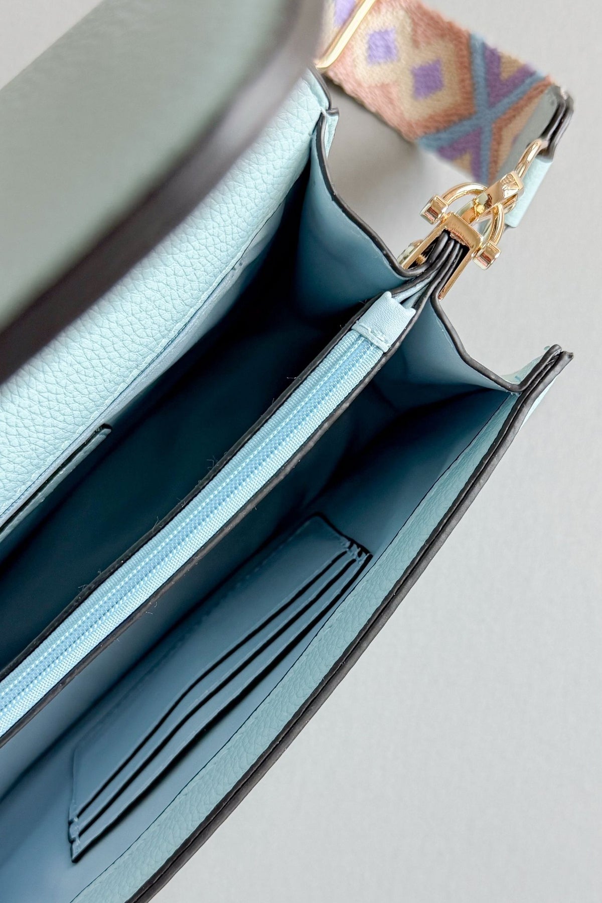 womens light blue handbag with a purple, taupe and blue patterned adjustable guitar strap on a grey background showing inside card slots, middle zippper and 2 open storage areas