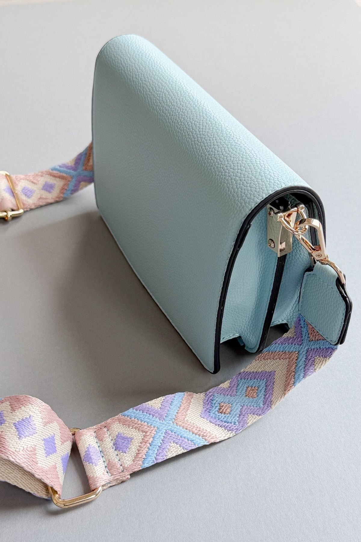 womens light blue handbag with a purple, taupe and blue patterned adjustable guitar strap on a grey background