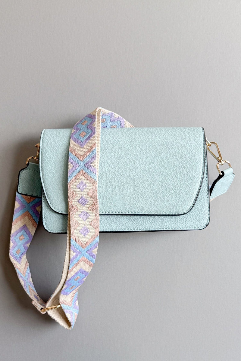 womens light blue handbag with a purple, taupe and blue patterned adjustable guitar strap on a grey background