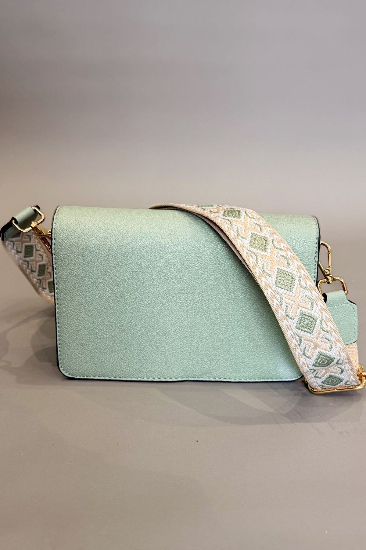 sage handbag with a patterned strap on a gray background
