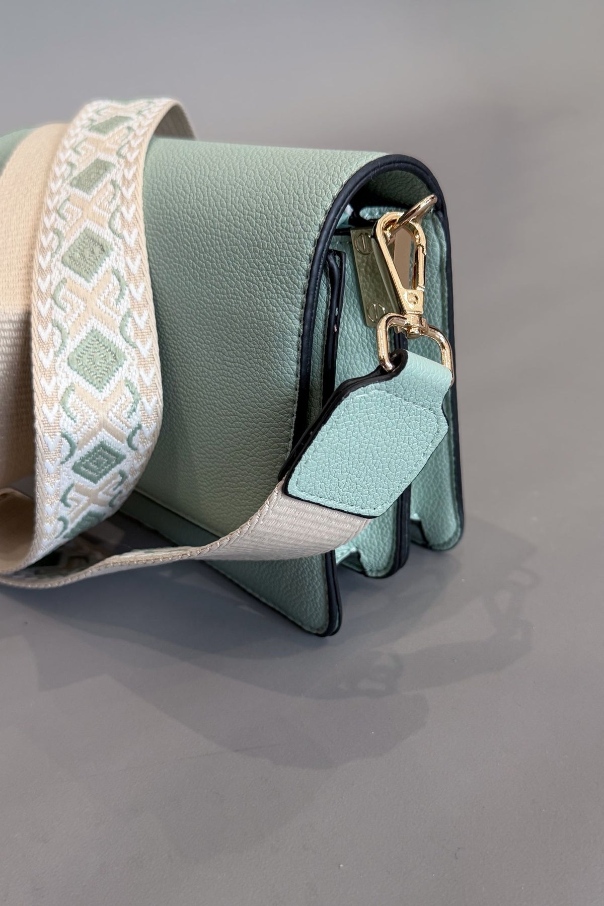 Green handbag with a patterned strap on a gray background
