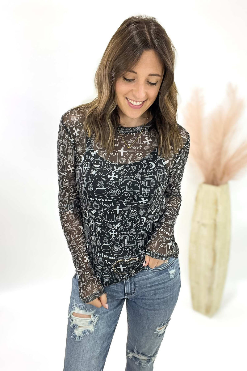 Woman wearing a black patterned long-sleeve top and jeans on a white background
