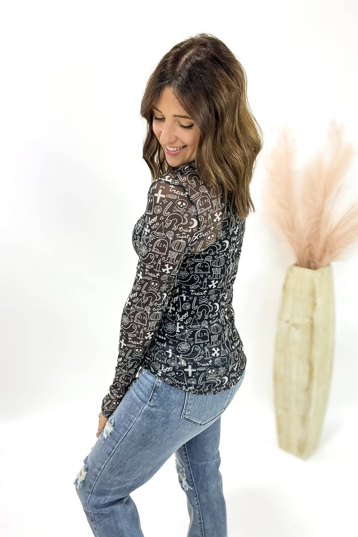 Woman wearing a patterned long-sleeve top and jeans against a white background