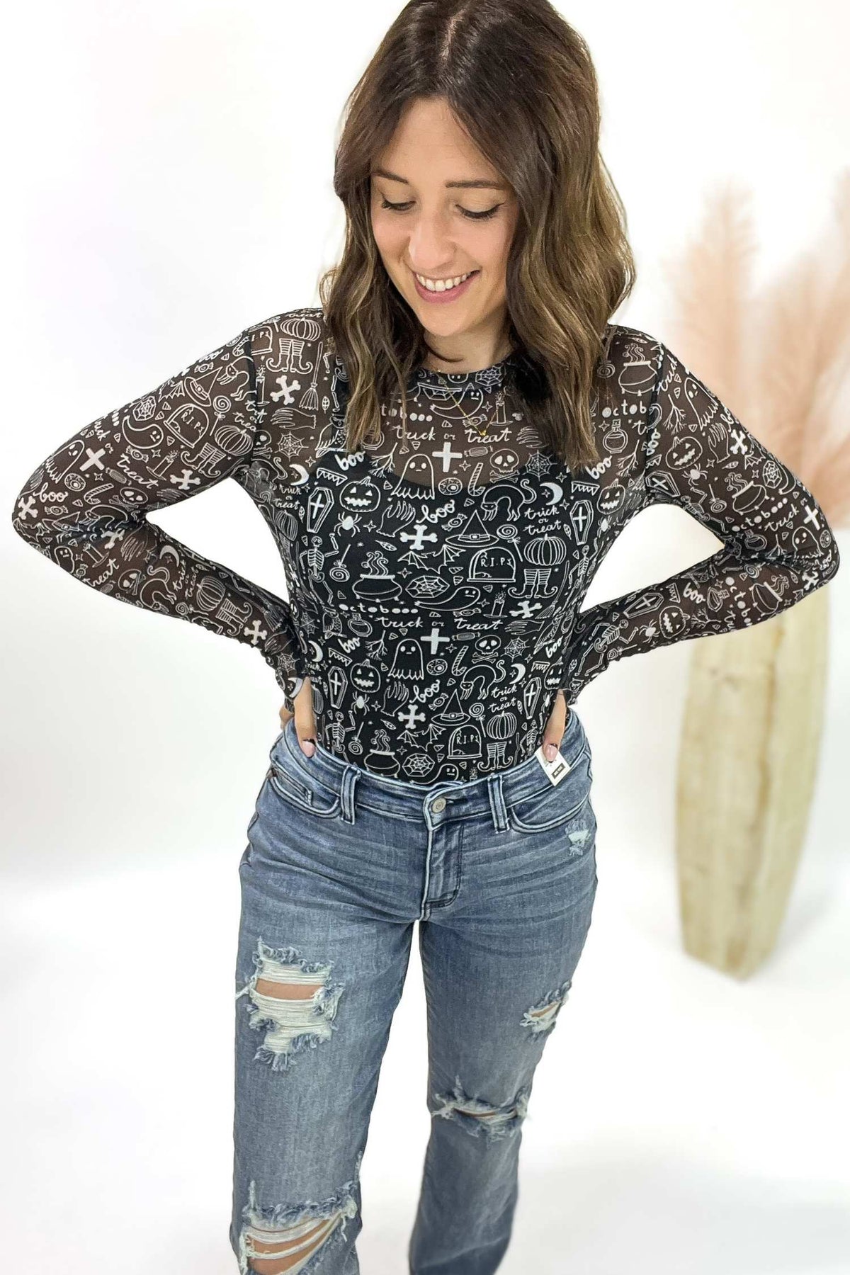 Woman wearing a black mesh top with patterns and blue jeans on a white background