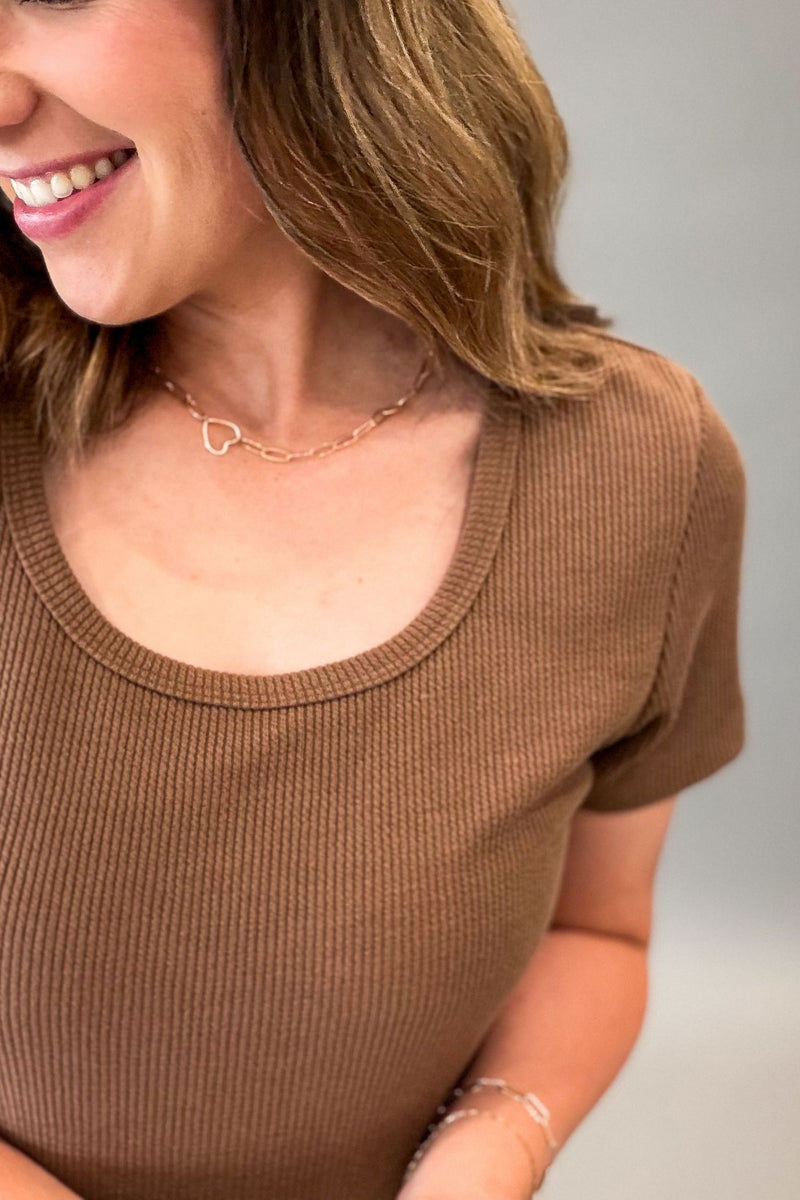 A close-up of a woman wearing a hazelnut ribbed short-sleeve scoop-neck top, showing her smiling and neck with a delicate gold necklace.