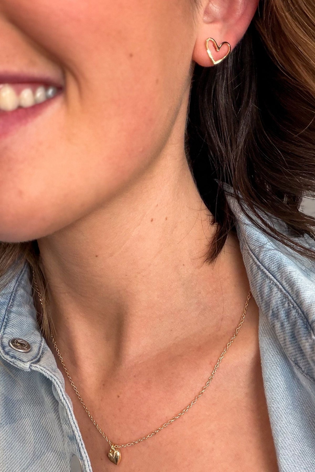 Close-up of a person wearing a gold heart-shaped earring and necklace.