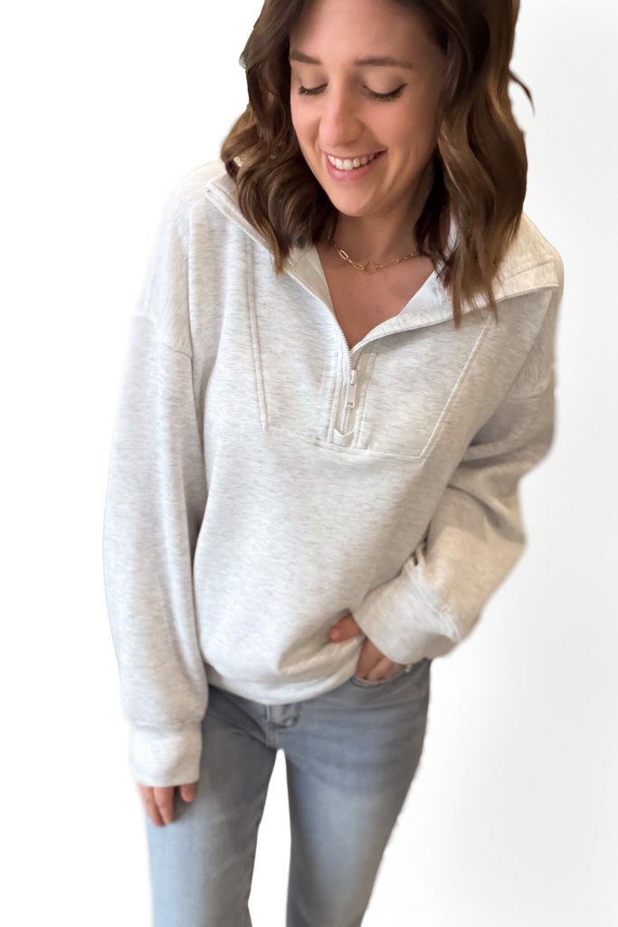 Woman wearing a light gray zip-up sweatshirt and light blue jeans on a white background