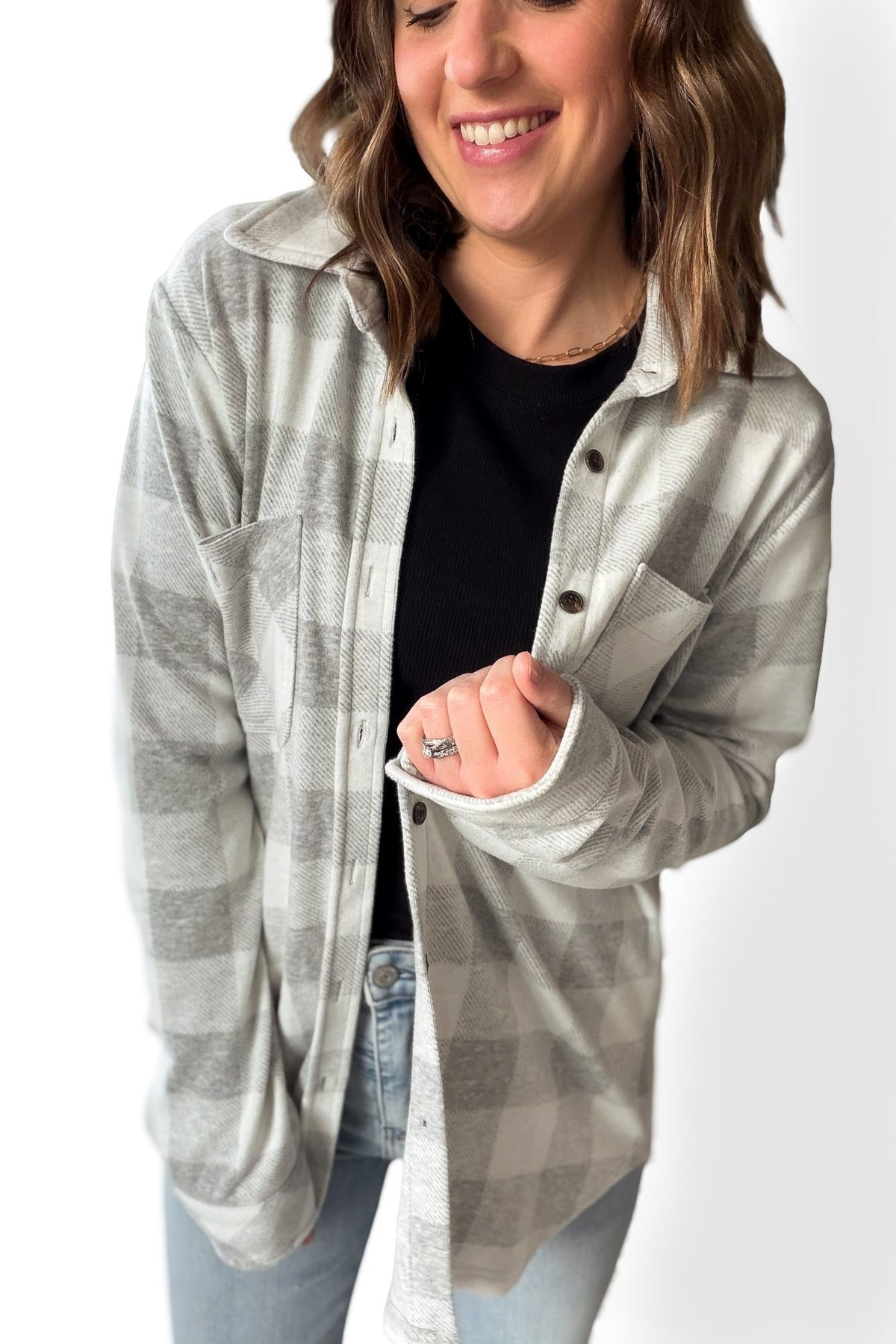 Woman wearing a gray checkered button up over a black top on a white background