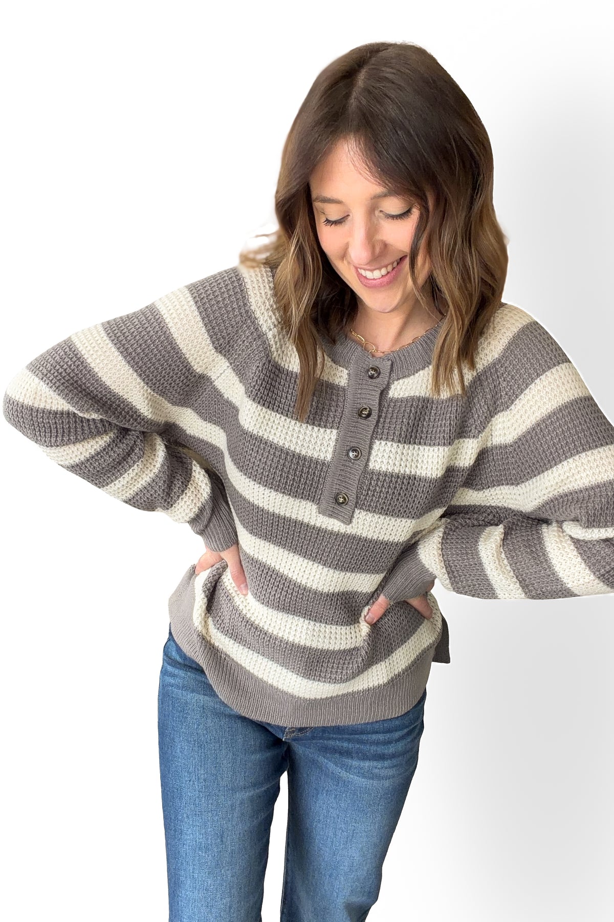 Woman wearing a gray and white striped sweater with blue jeans on a white background