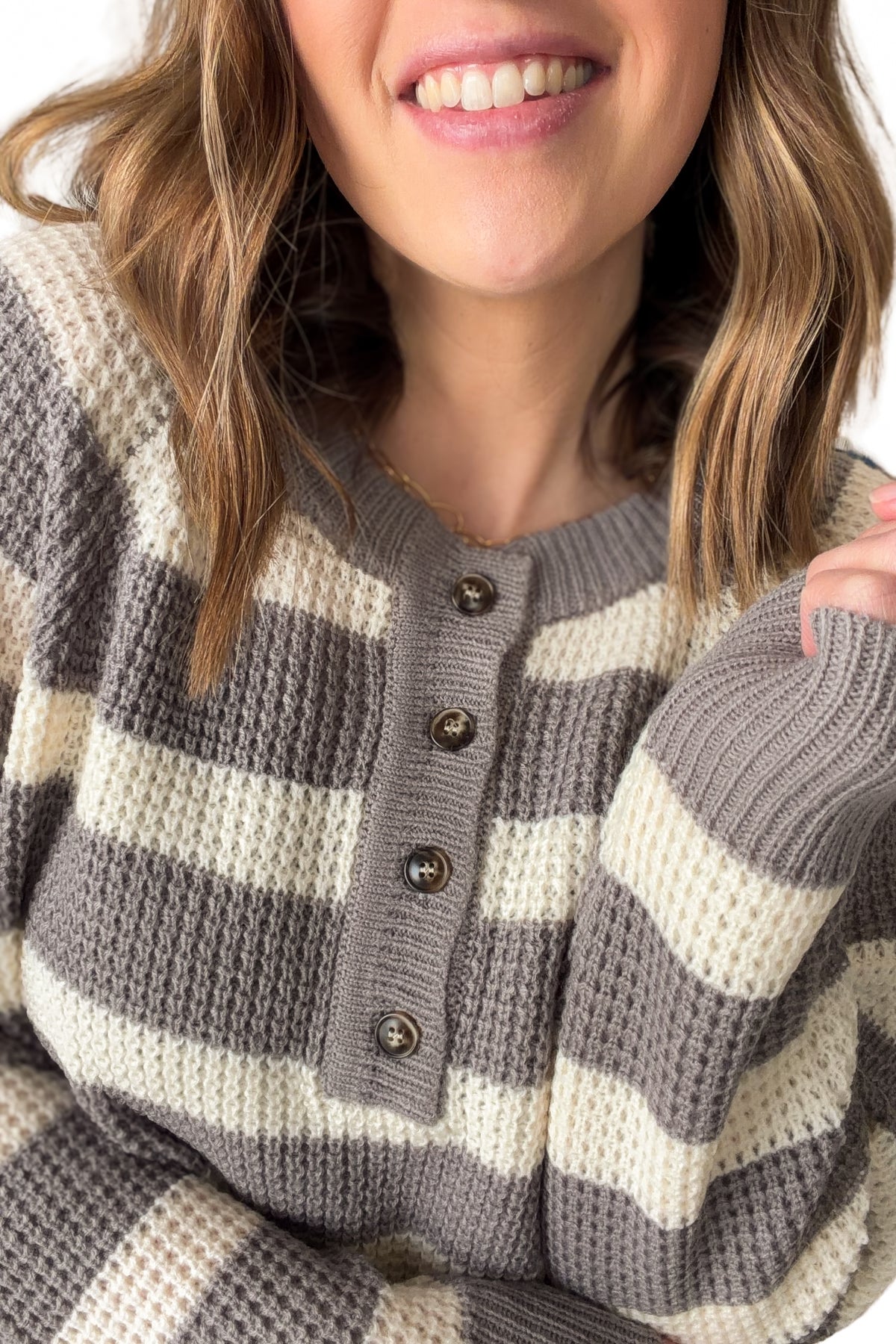 Close-up of a person wearing a gray and white striped sweater with buttons.