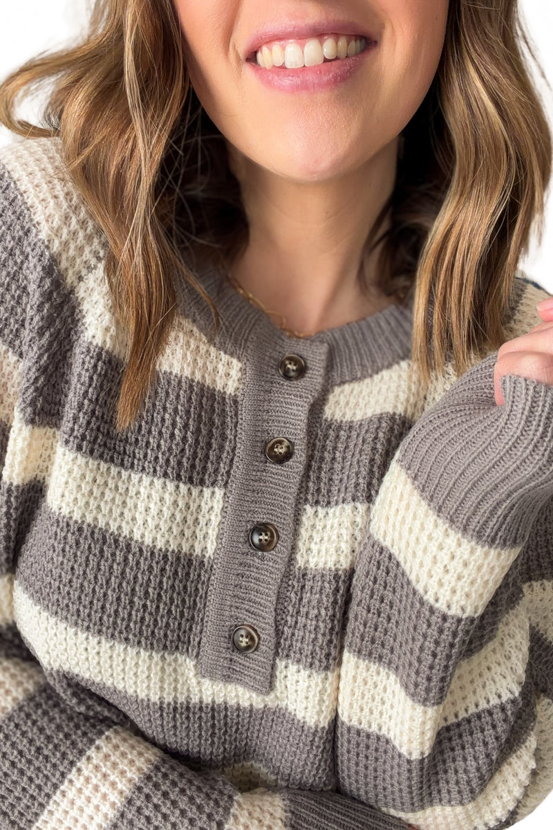 Close-up of a person wearing a gray and white striped sweater with buttons.