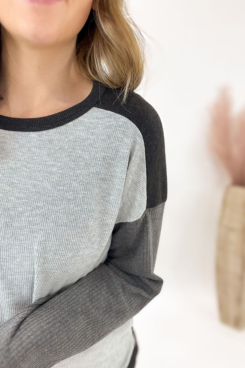 Gray and black long-sleeve shirt worn by a person on a white background