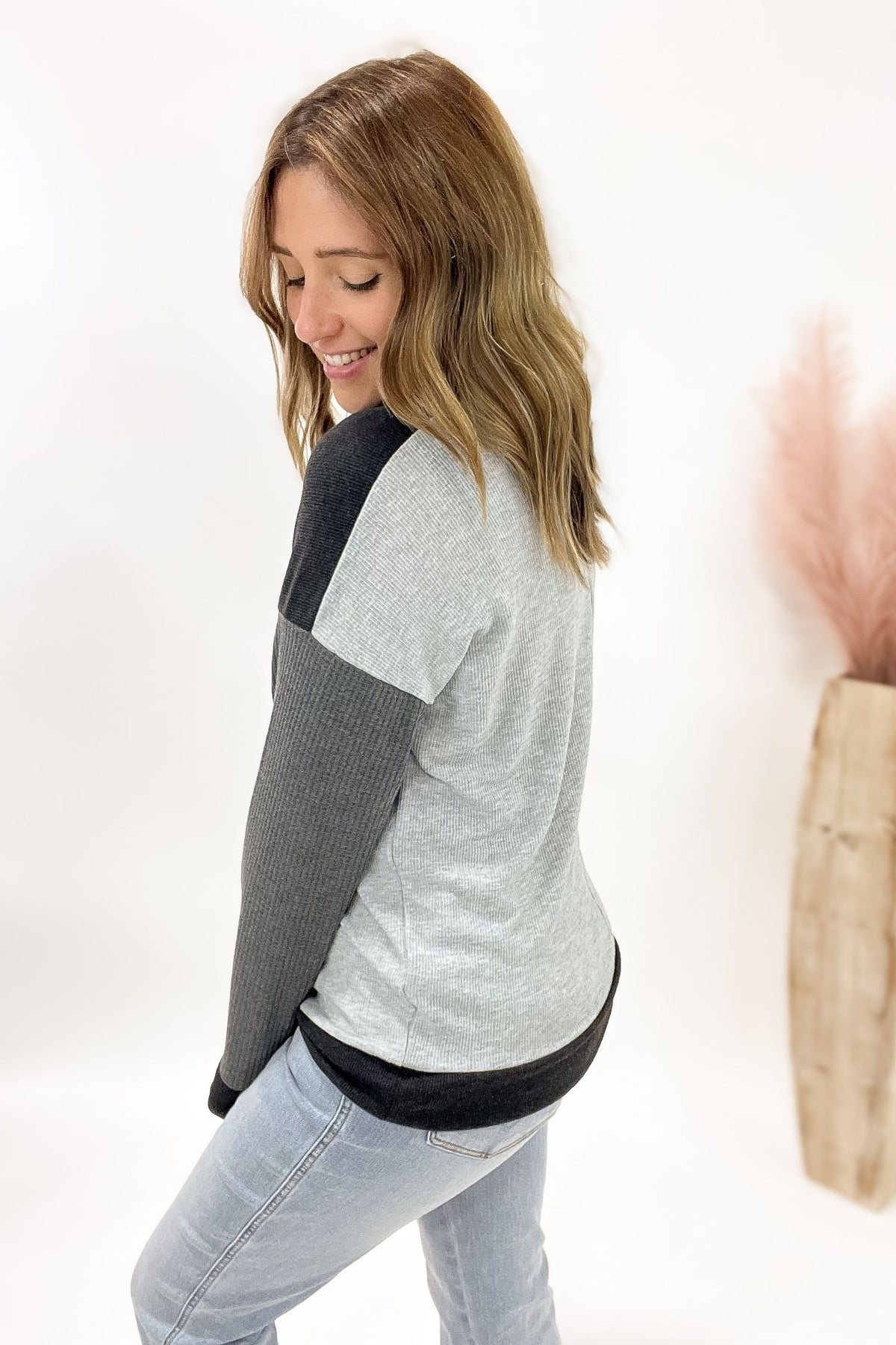 Woman wearing a gray and black color-blocked sweater with light blue jeans on a white background