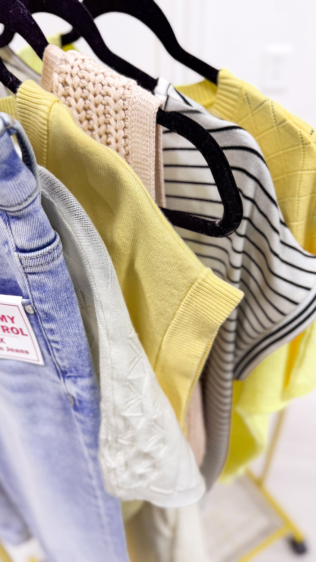 Clothing items including a yellow sweater, striped shirt, and jeans on hangers.