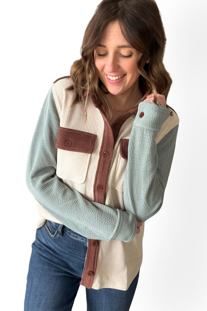 Woman wearing a colorblock shacket with green, brown, and beige colors on a white background