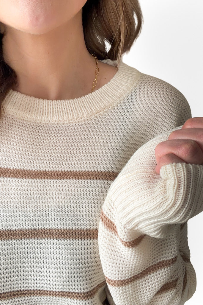 Close-up of a person wearing a cream-colored sweater with brown stripes.