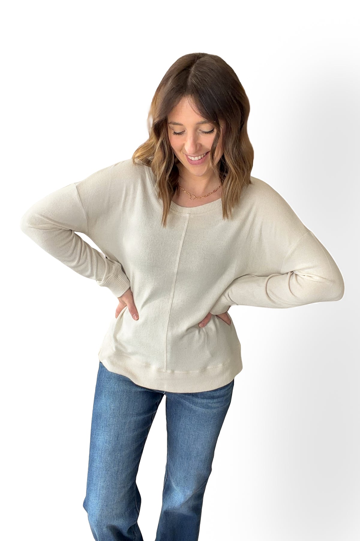 Woman wearing an ivory sweater and blue jeans on a white background