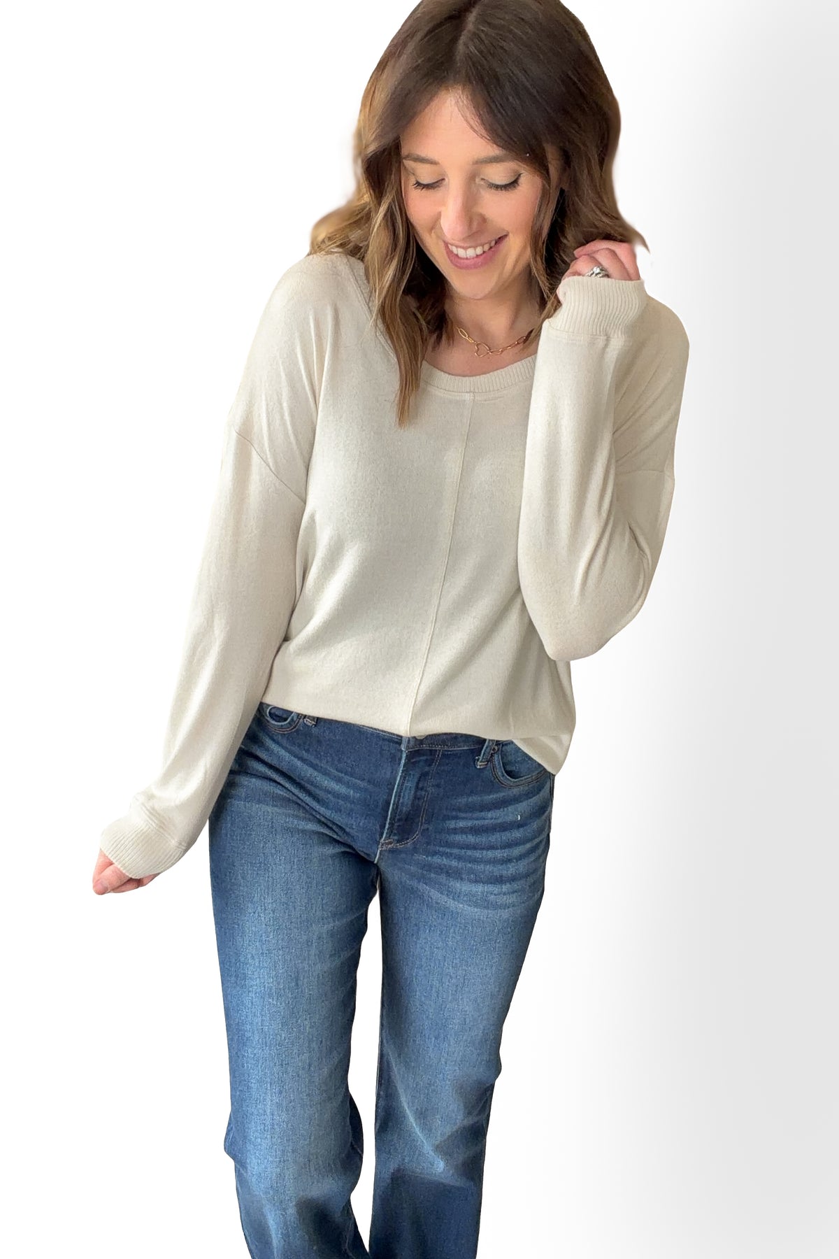 Woman wearing an ivory sweater and blue jeans on a white background