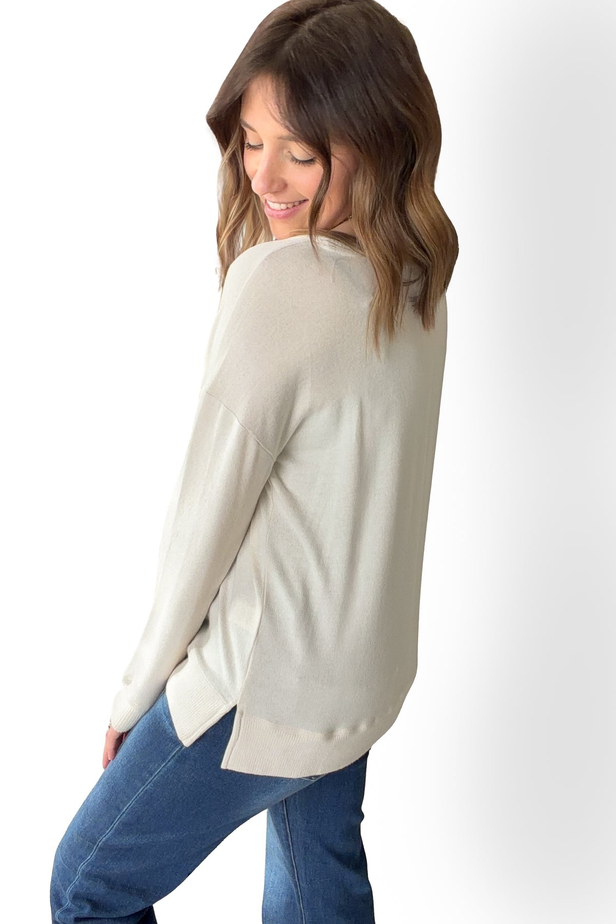 Woman wearing a ivory long-sleeve top and blue jeans on a white background