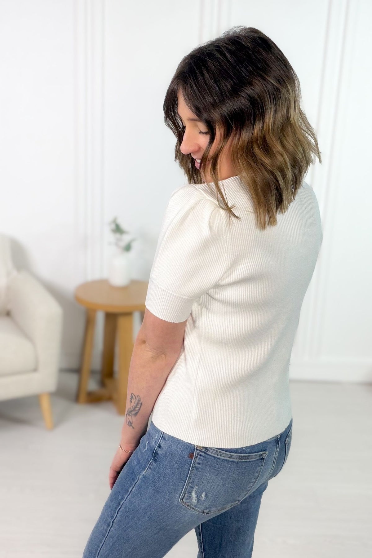 Woman wearing a white sweater and blue jeans in a minimalistic room.