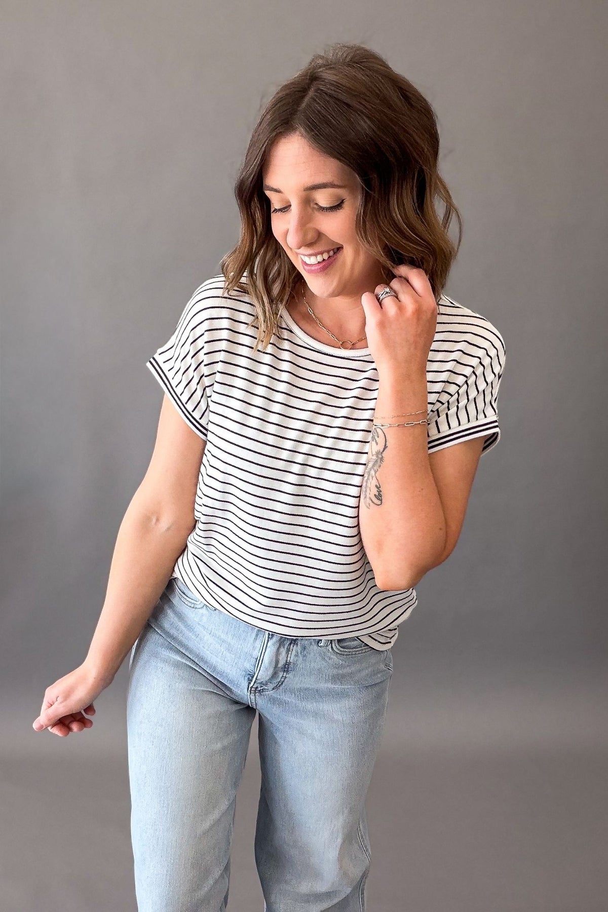 Woman wearing a striped shirt and light blue jeans against a gray background