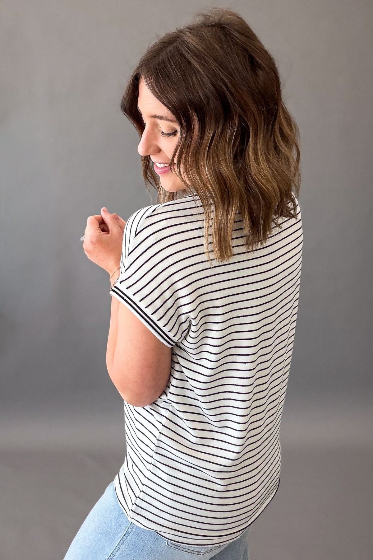 Woman wearing a striped shirt and jeans against a gray background