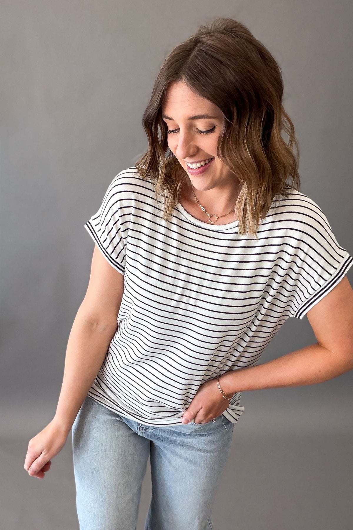 Woman wearing a striped shirt and jeans against a gray background