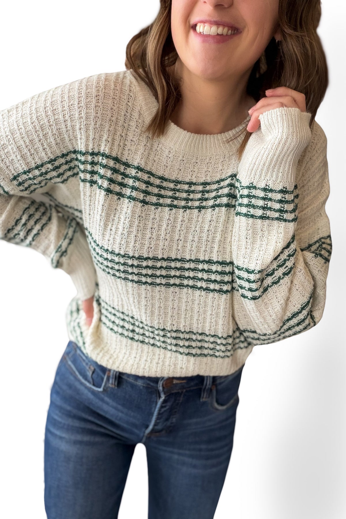 Person wearing a cream sweater with green stripes and blue jeans on a white background