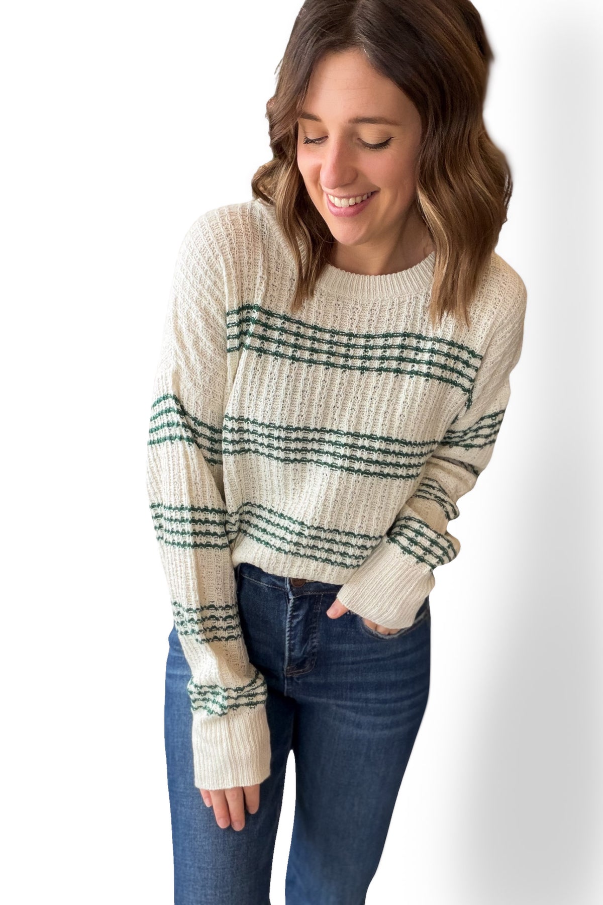 Woman wearing a cream sweater with green stripes and blue jeans on a white background