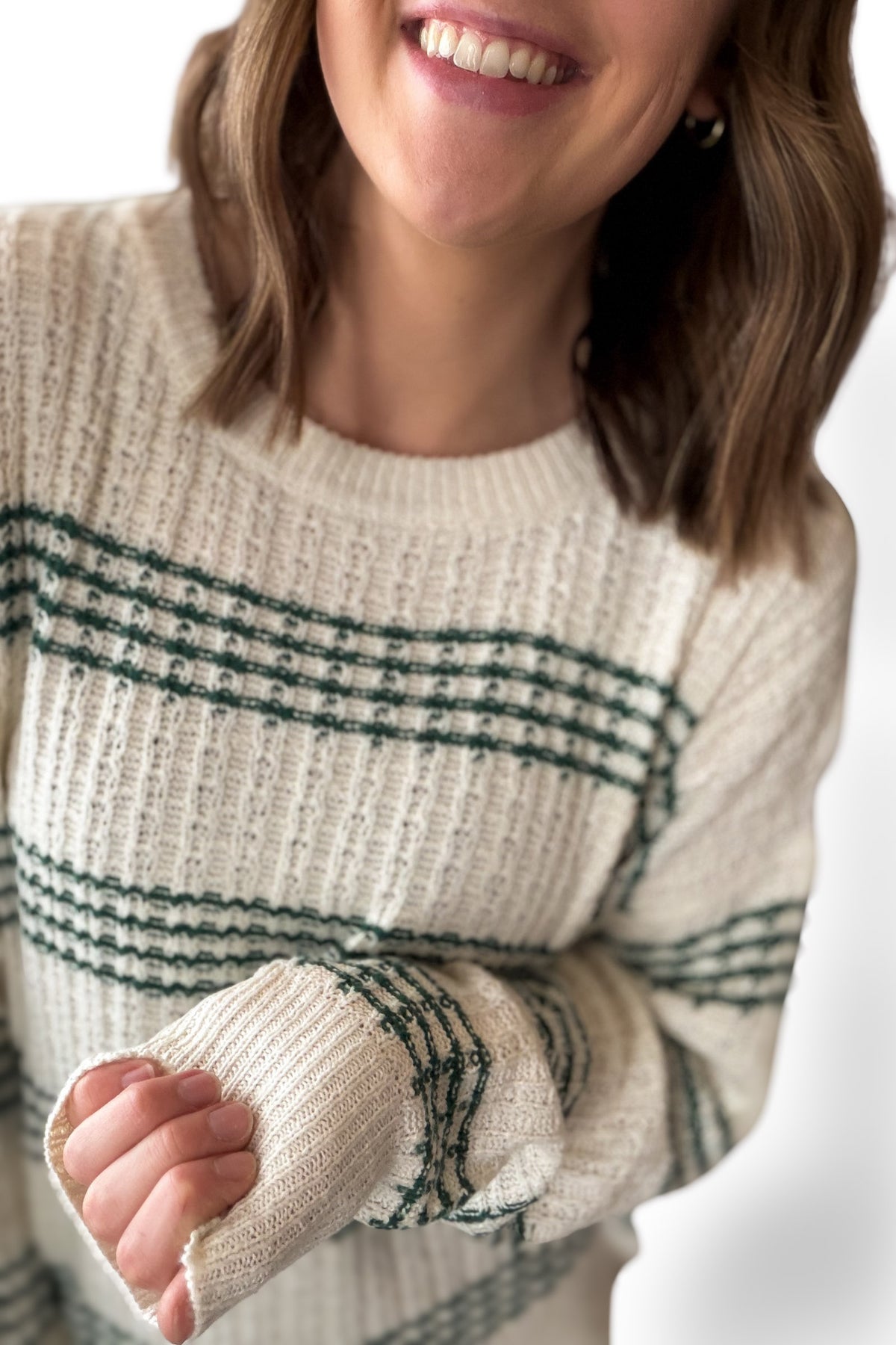 Person wearing a cream sweater with green pattern on a white background