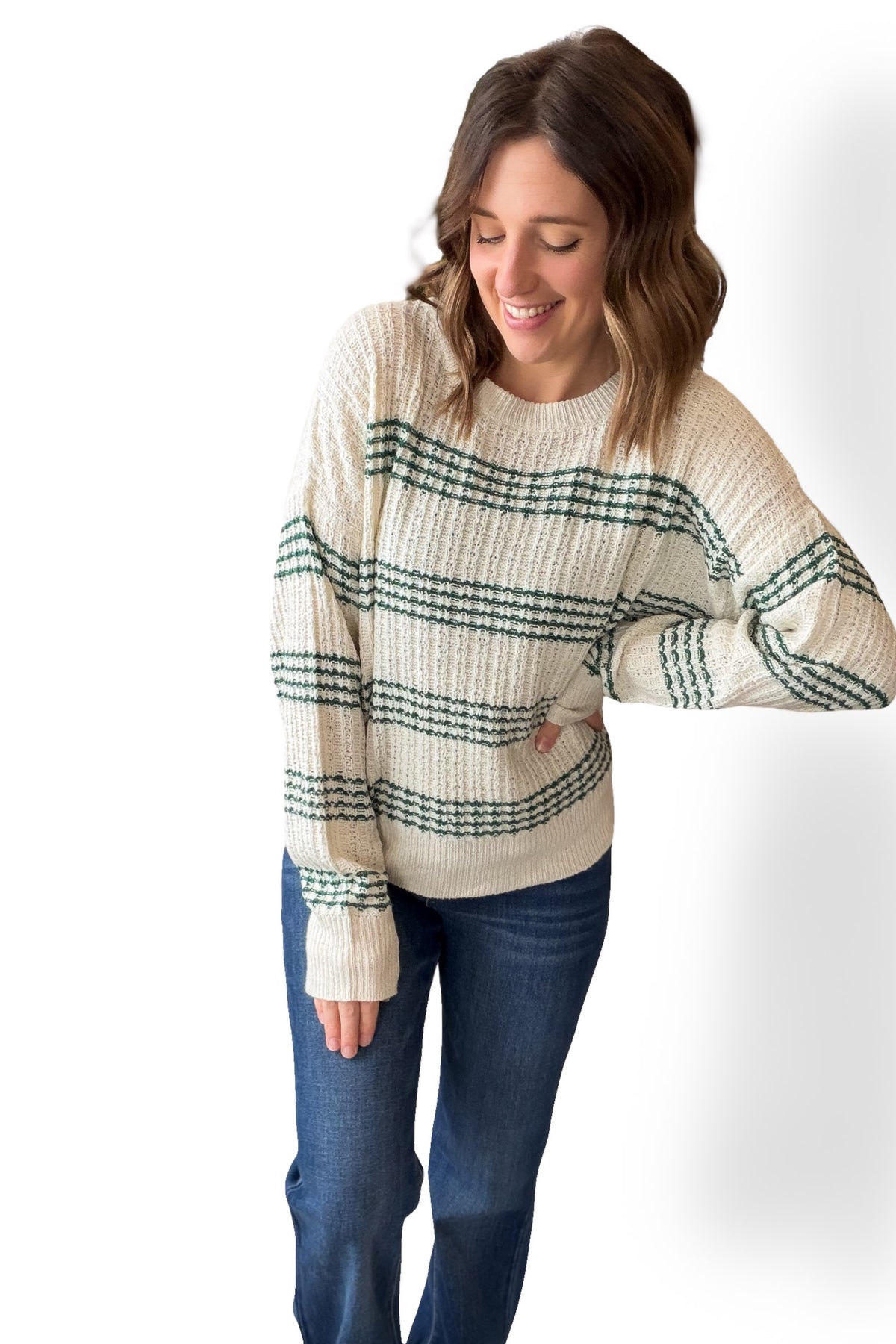 Woman wearing a cream and green striped sweater with blue jeans on a white background