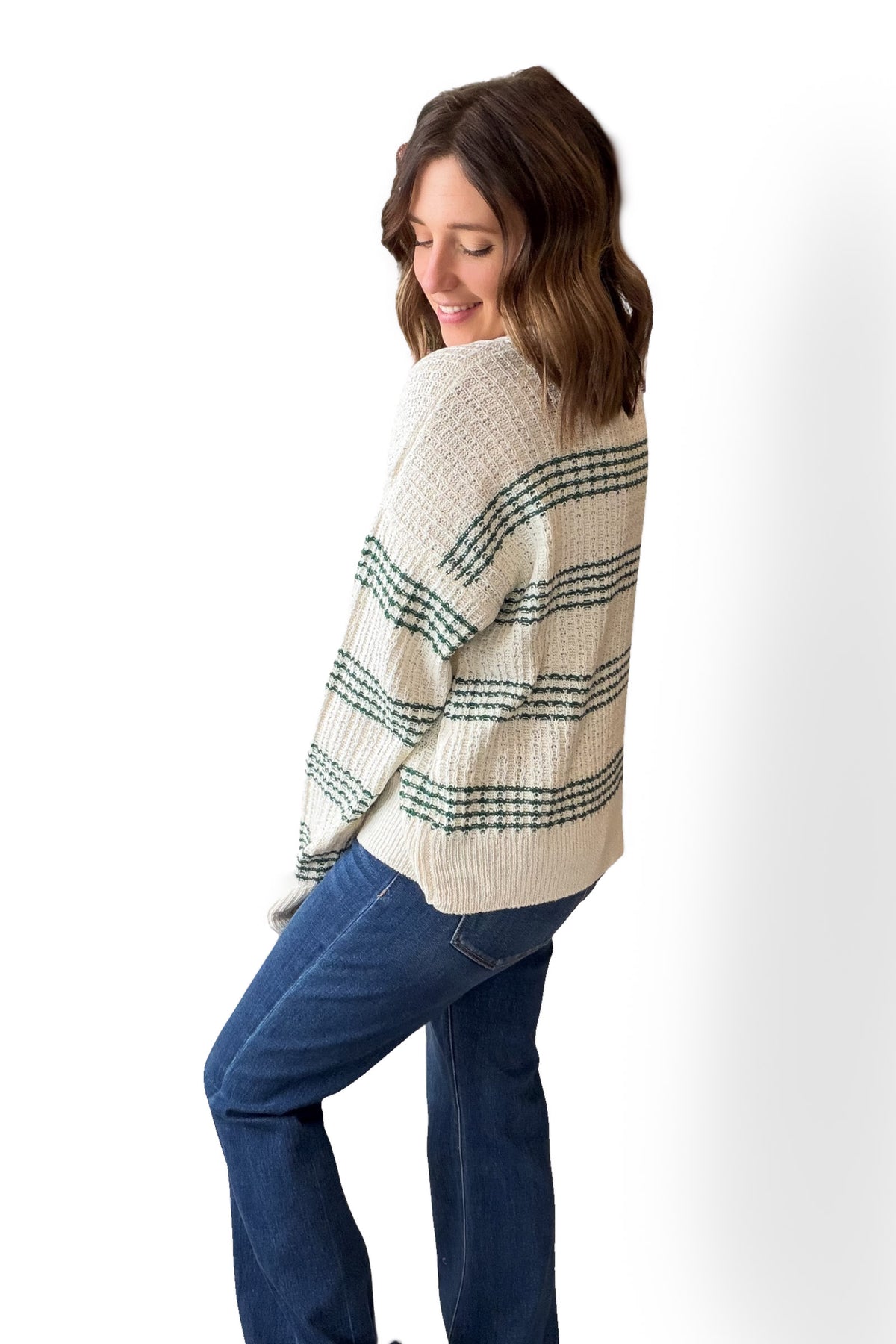 Woman wearing a cream sweater with black stripes and blue jeans on a white background
