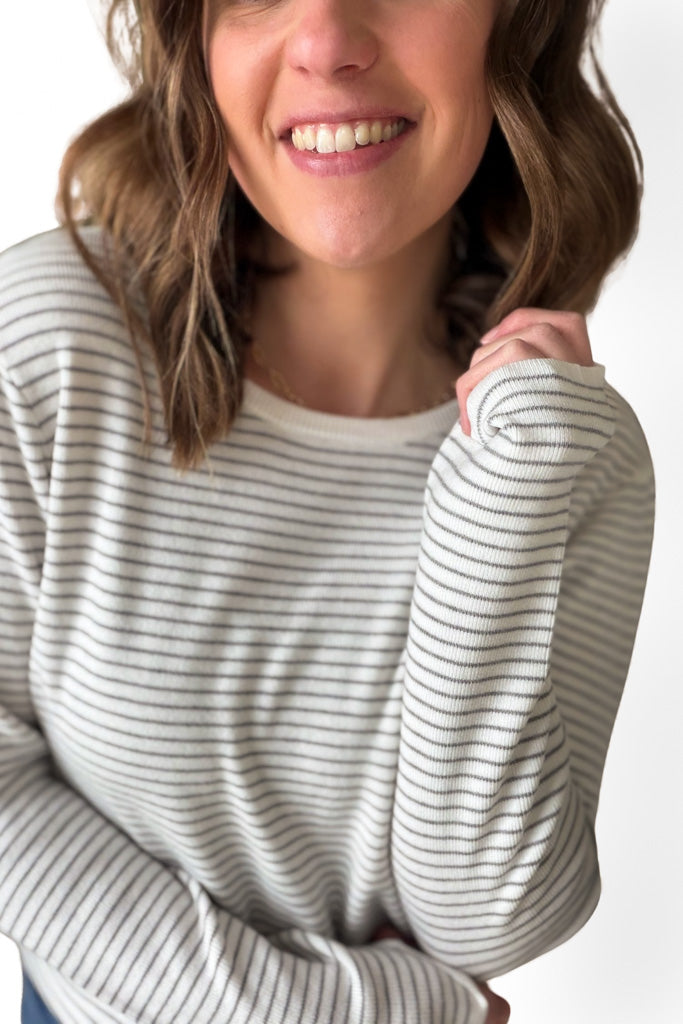 Person wearing a white and gray striped long-sleeve shirt on a plain background