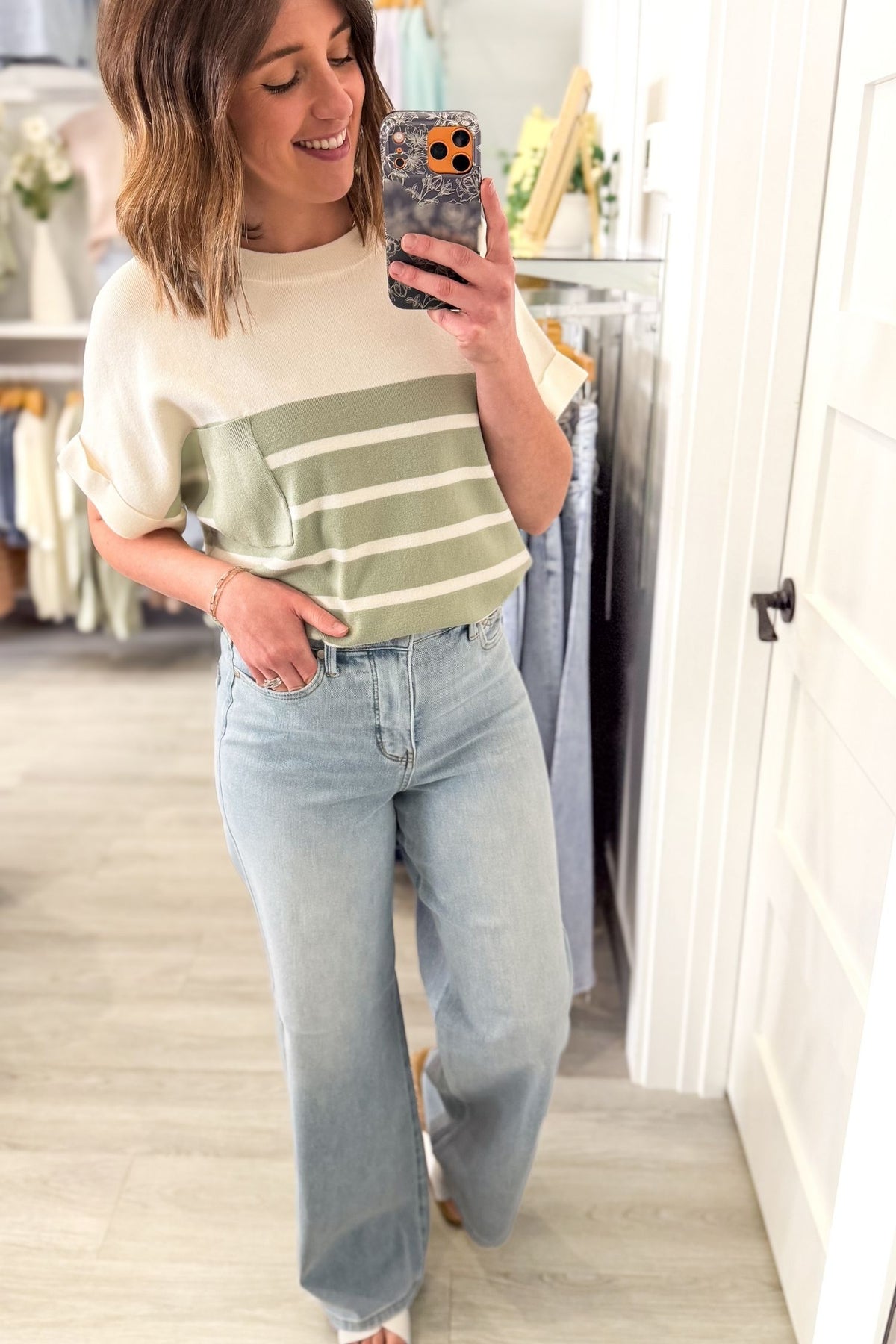 Woman wearing an ivory short sleeve knit top with sage stripes, rolled sleeve cuffs, chest pocket, and light wash jeans